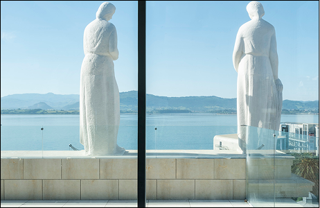 Esculturas alegóricas restauradas de José Planes en la terraza de Faro Santander con vistas panorámicas a la bahía.